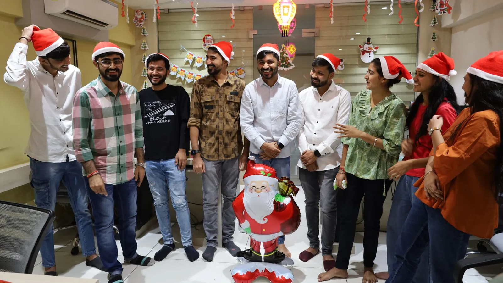 Team members in Santa hats laughing around a Santa balloon at the office