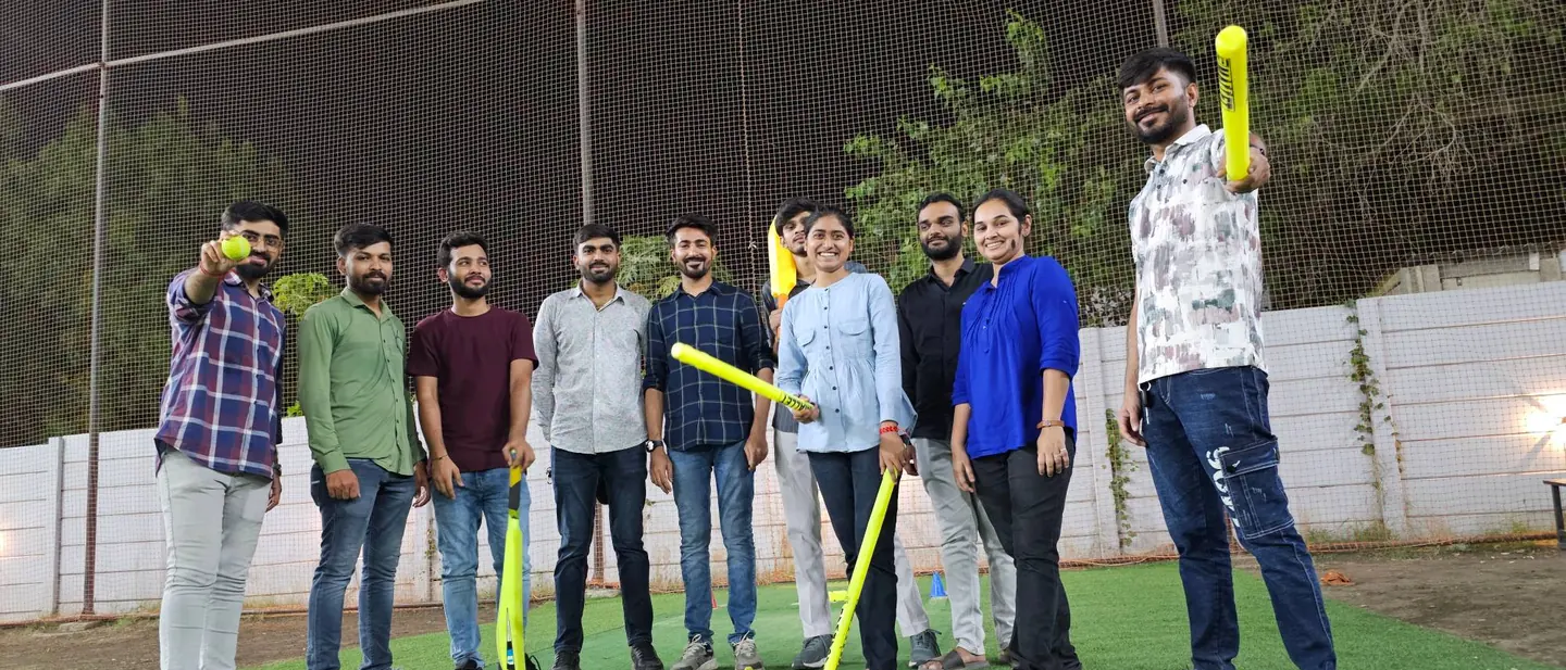 The TeqStars team with bats and a ball at a floodlit cricket net